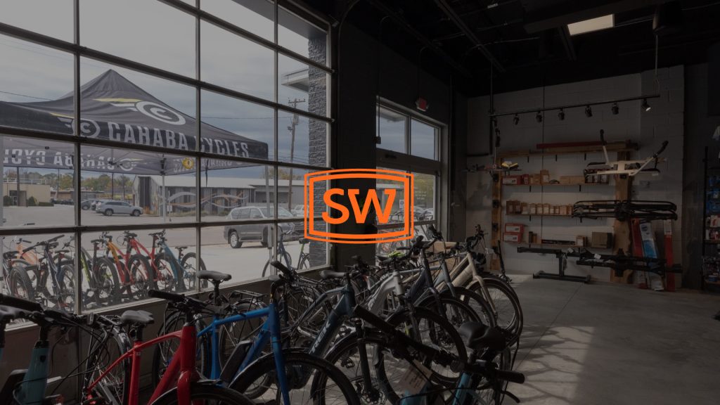 Shannon Waltchack logo over a photo of the inside of a bike shop