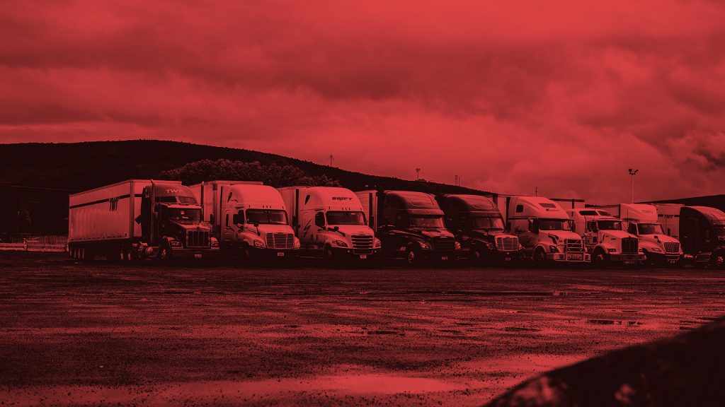 A line of tank trucks sitting in a gravel field. the entire photo has a red tint overlay